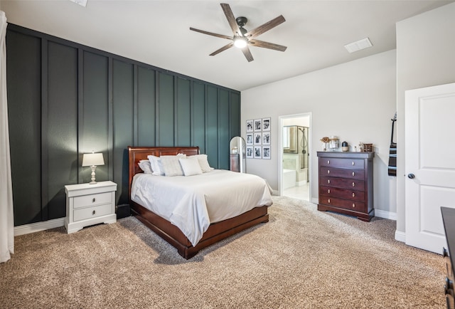 carpeted bedroom featuring visible vents, a decorative wall, a ceiling fan, ensuite bath, and baseboards