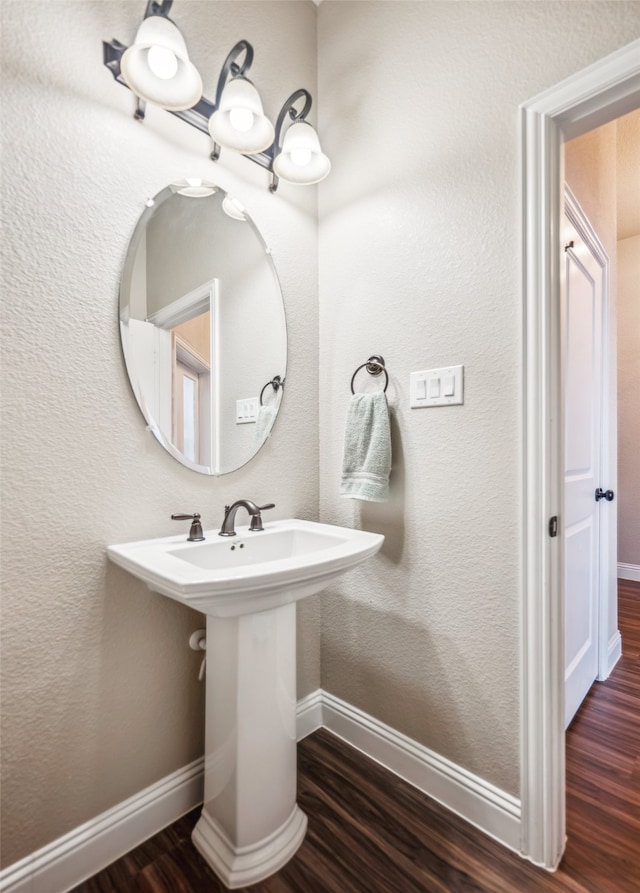 bathroom with a sink, a textured wall, wood finished floors, and baseboards