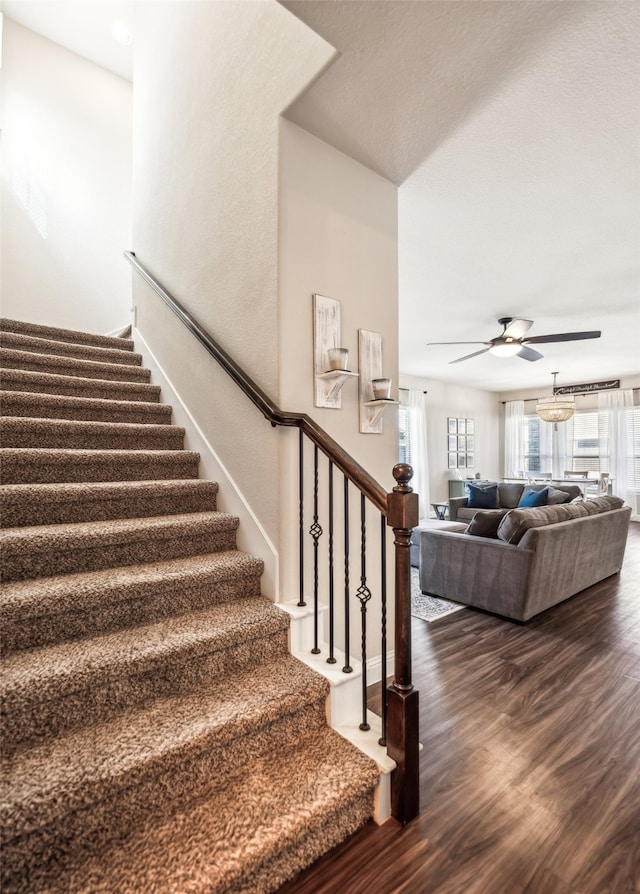 staircase featuring wood finished floors, a ceiling fan, and baseboards