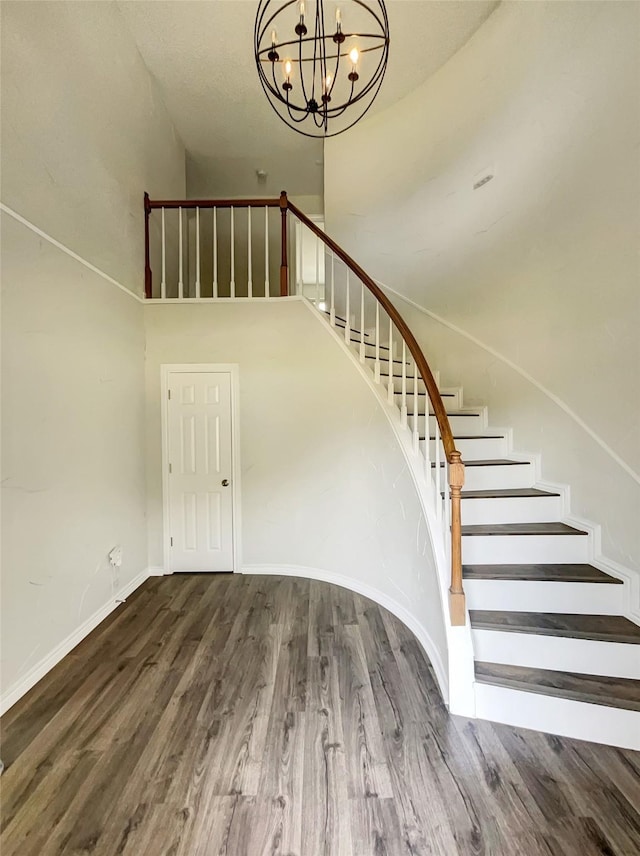 staircase featuring a towering ceiling, an inviting chandelier, baseboards, and wood finished floors