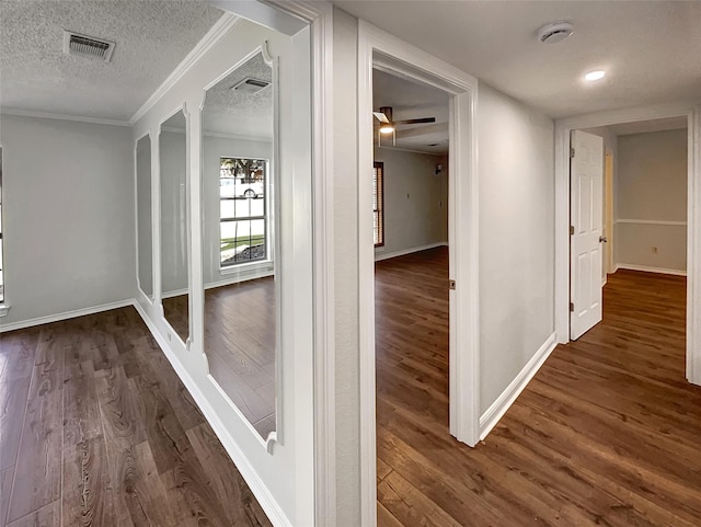 hallway featuring dark wood-style flooring, crown molding, visible vents, a textured ceiling, and baseboards