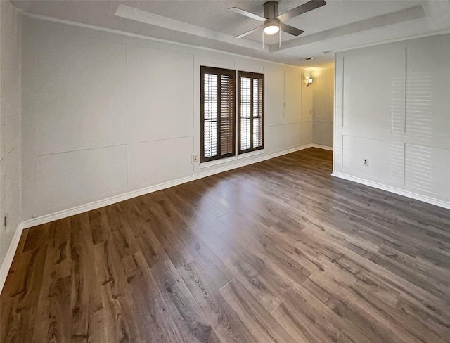 empty room featuring ceiling fan, a raised ceiling, wood finished floors, and a decorative wall