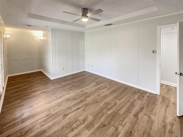 spare room featuring a textured ceiling, wood finished floors, a raised ceiling, and a decorative wall