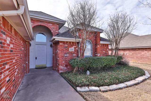 doorway to property featuring brick siding and a shingled roof