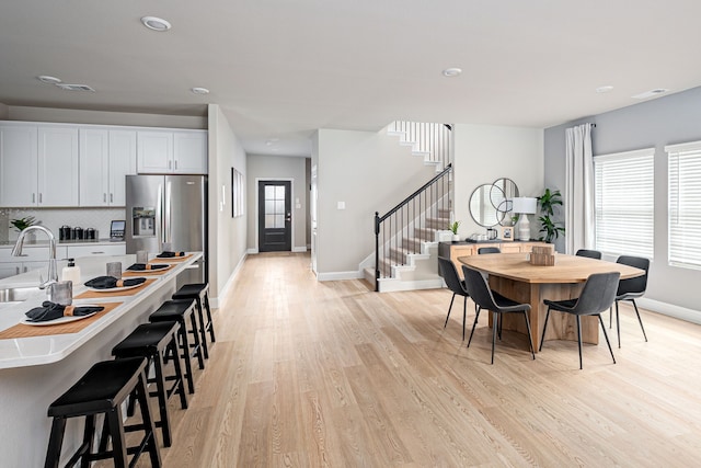 dining space with stairway, light wood-type flooring, visible vents, and baseboards