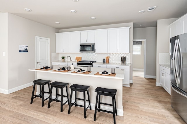 kitchen featuring stainless steel appliances, a kitchen bar, visible vents, and decorative backsplash