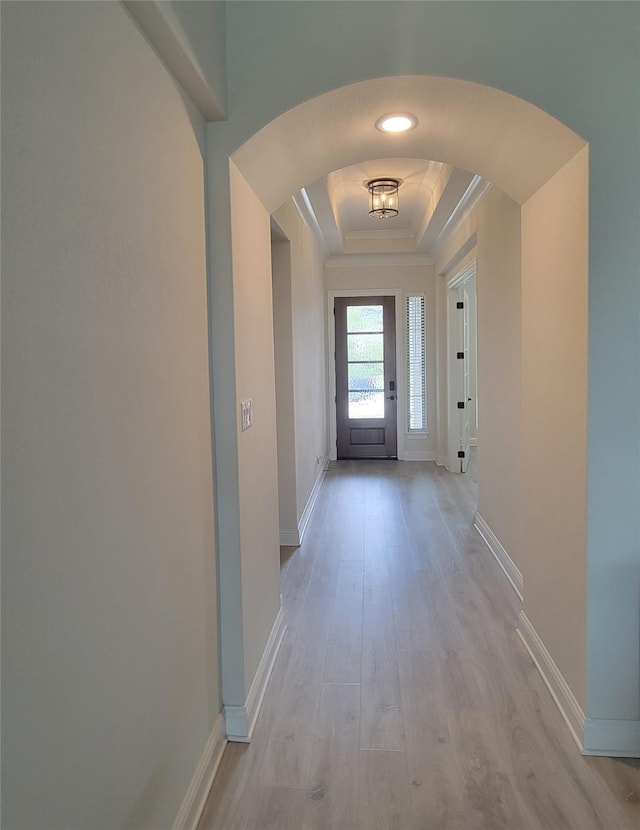 doorway to outside with arched walkways, baseboards, light wood finished floors, ornamental molding, and a tray ceiling