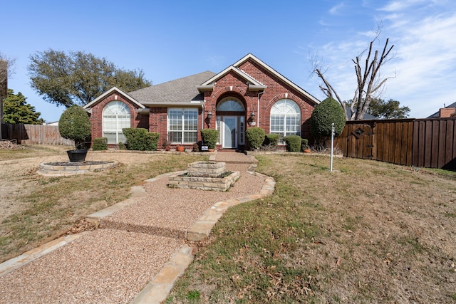 ranch-style home featuring roof with shingles, a front yard, fence, and brick siding