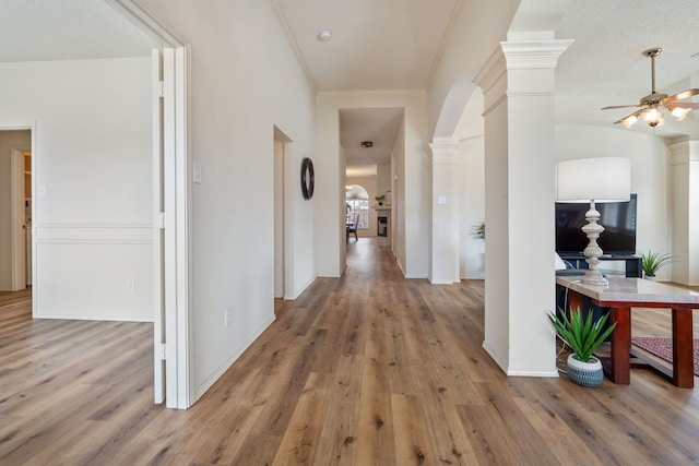 hall with arched walkways, wood finished floors, baseboards, ornamental molding, and decorative columns