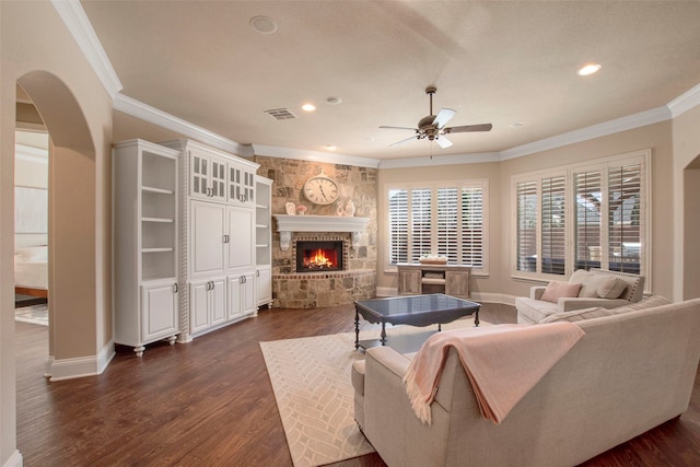 living area with visible vents, dark wood-type flooring, ornamental molding, arched walkways, and a stone fireplace