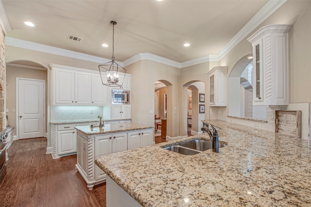 kitchen with stainless steel microwave, a center island with sink, white cabinetry, and a sink