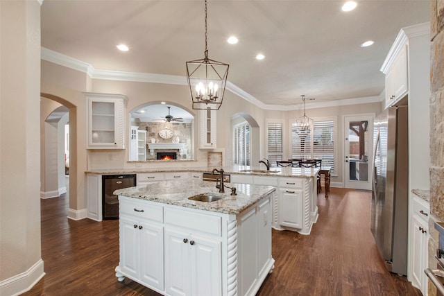 kitchen with an island with sink, arched walkways, freestanding refrigerator, a sink, and wine cooler