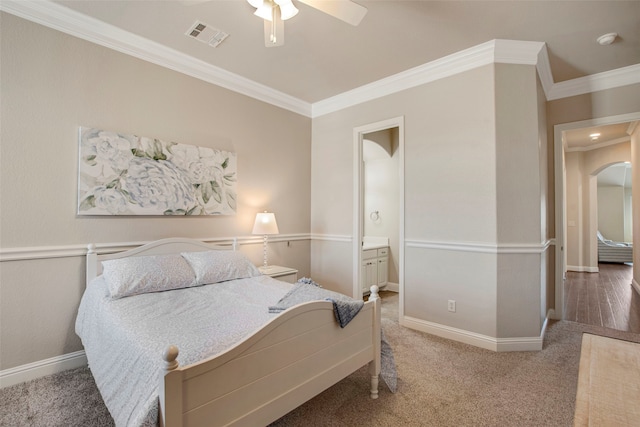 carpeted bedroom with visible vents, crown molding, baseboards, arched walkways, and ensuite bath