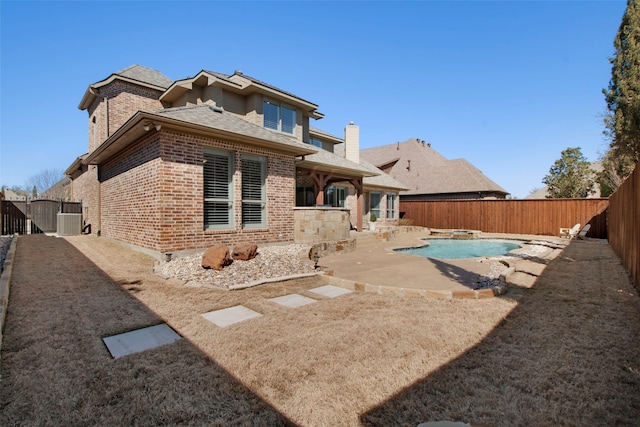 back of property with brick siding, a patio area, a fenced backyard, and a fenced in pool