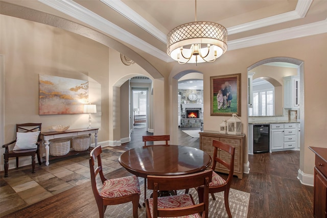 dining space featuring crown molding, beverage cooler, dark wood finished floors, a notable chandelier, and a raised ceiling