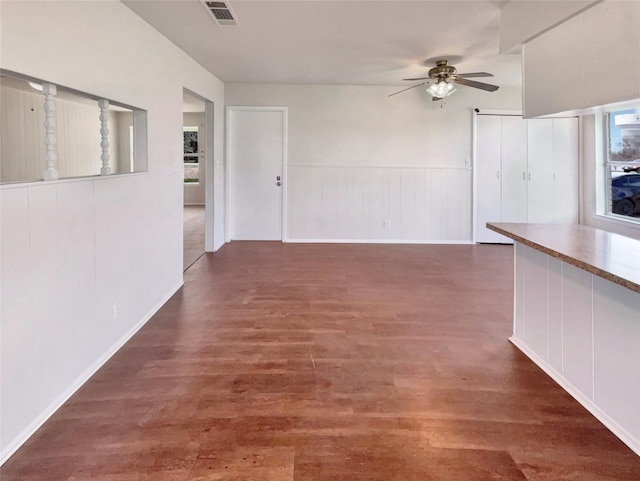 unfurnished living room with ceiling fan, wainscoting, wood finished floors, and visible vents