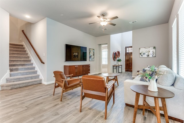 living room featuring baseboards, visible vents, a ceiling fan, stairs, and light wood-style floors