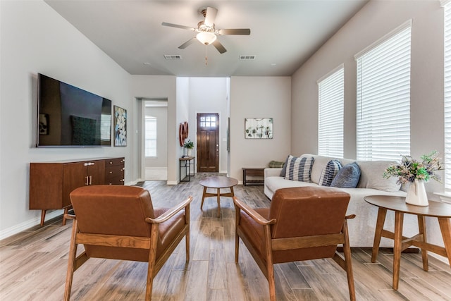 living room with ceiling fan, light wood-style flooring, visible vents, and baseboards