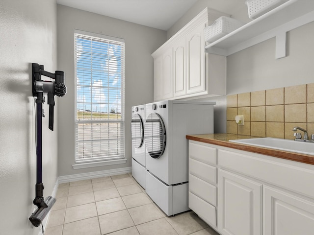 laundry area featuring light tile patterned floors, baseboards, washing machine and clothes dryer, cabinet space, and a sink