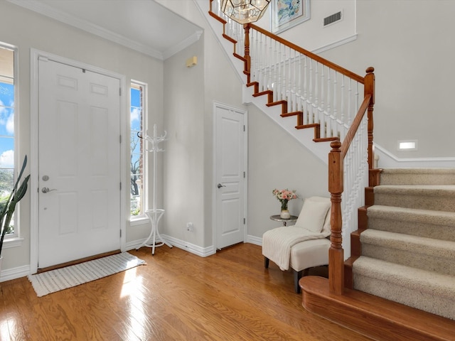 foyer entrance with visible vents, wood finished floors, stairway, crown molding, and baseboards