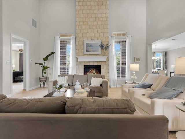 carpeted living room featuring visible vents, baseboards, a stone fireplace, a high ceiling, and an inviting chandelier