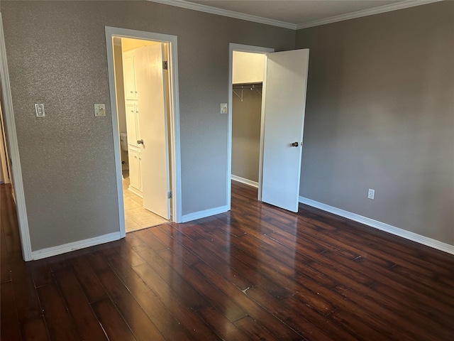 unfurnished bedroom featuring a walk in closet, dark wood-style flooring, a closet, ornamental molding, and baseboards