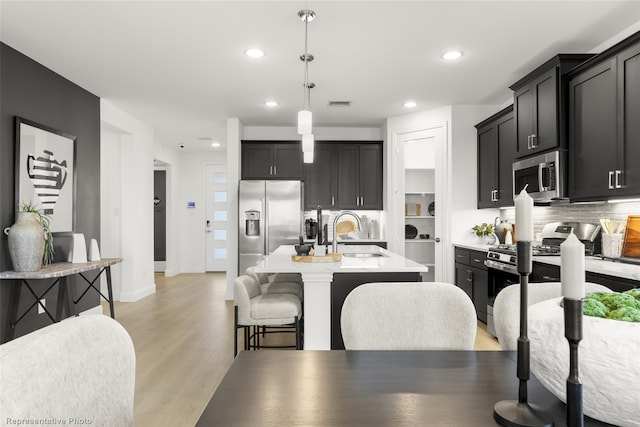 kitchen featuring stainless steel appliances, light countertops, backsplash, light wood-style flooring, and a sink