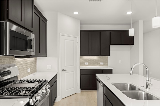 kitchen with light stone counters, stainless steel appliances, hanging light fixtures, light wood-style flooring, and a sink