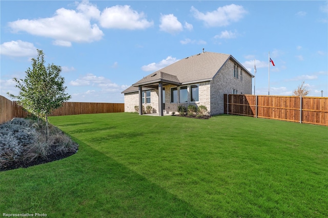 back of house featuring a yard, brick siding, roof with shingles, and a fenced backyard