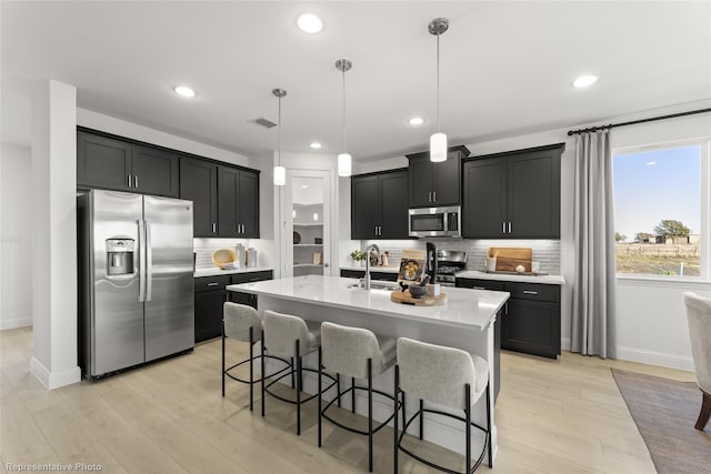 kitchen with light wood-style flooring, appliances with stainless steel finishes, dark cabinets, a kitchen bar, and backsplash