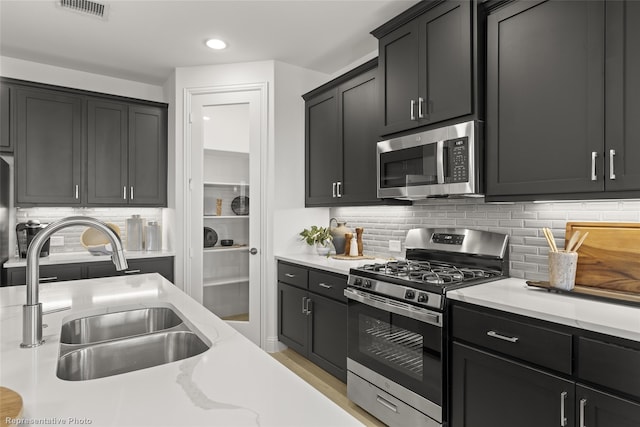 kitchen with stainless steel appliances, visible vents, backsplash, a sink, and light stone countertops