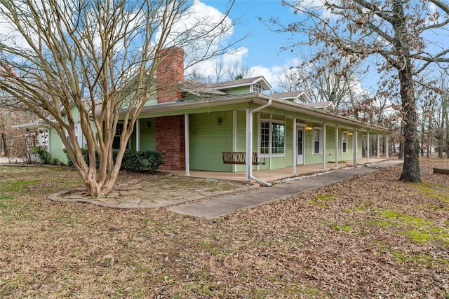 view of front of property with covered porch, brick siding, and a chimney