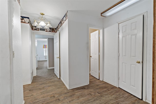 hall with baseboards, an inviting chandelier, and wood finished floors