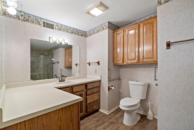 bathroom featuring visible vents, toilet, vanity, wood finished floors, and tiled shower