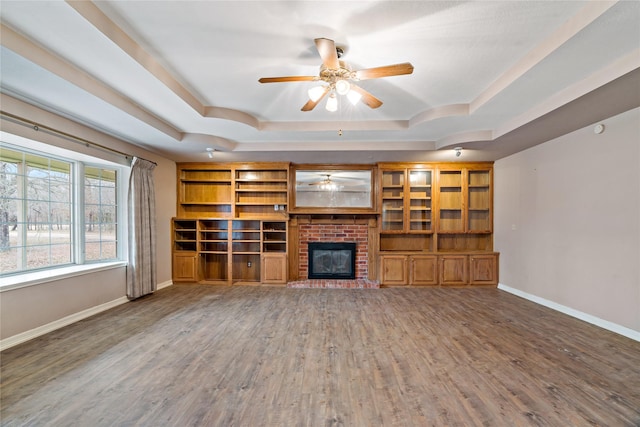 unfurnished living room featuring a tray ceiling, wood finished floors, and baseboards