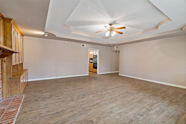 unfurnished living room featuring visible vents, baseboards, a raised ceiling, ceiling fan, and wood finished floors