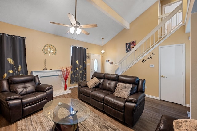 living area with lofted ceiling with beams, ceiling fan, wood finished floors, baseboards, and stairs