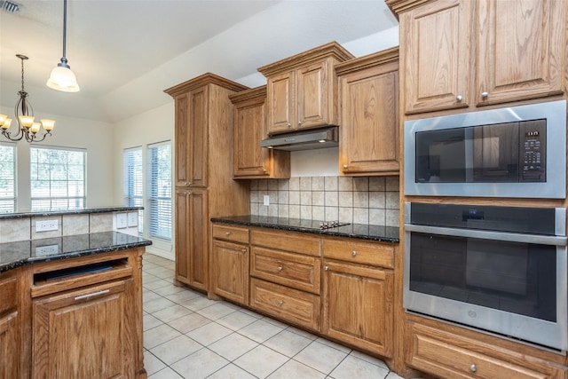 kitchen featuring oven, under cabinet range hood, built in microwave, backsplash, and brown cabinets