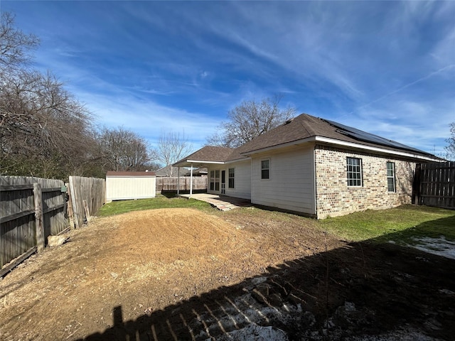 exterior space featuring an outbuilding, brick siding, roof mounted solar panels, a shed, and a fenced backyard