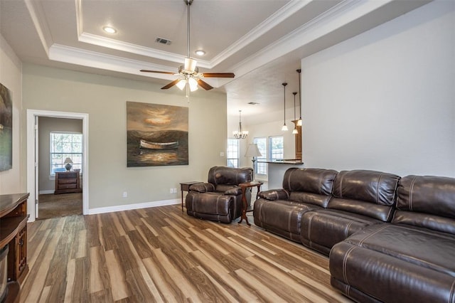 living room with wood finished floors, visible vents, baseboards, ornamental molding, and a tray ceiling