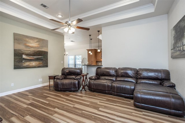 living area with a tray ceiling, crown molding, visible vents, light wood-type flooring, and baseboards