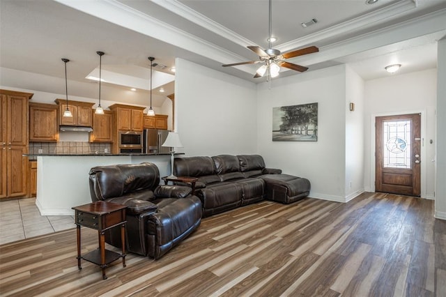 living area with a raised ceiling, visible vents, light wood-style floors, ornamental molding, and baseboards