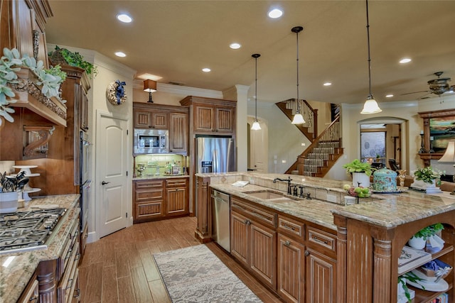 kitchen with a sink, ornamental molding, appliances with stainless steel finishes, light wood-type flooring, and brown cabinets