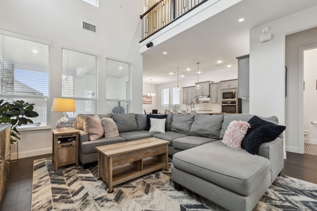 living room featuring a notable chandelier, baseboards, visible vents, and wood finished floors