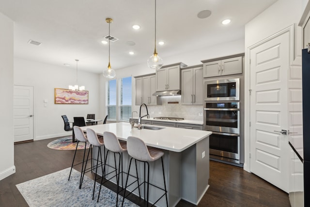 kitchen with a breakfast bar, tasteful backsplash, gray cabinets, appliances with stainless steel finishes, and a sink