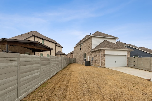 view of home's exterior with driveway, brick siding, central AC, and a fenced backyard