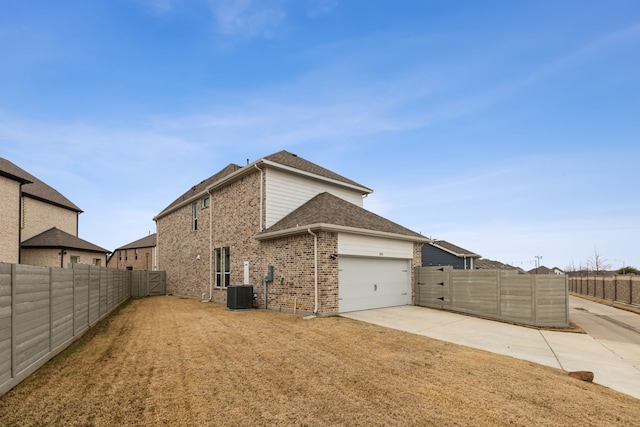 view of side of home featuring an attached garage, fence private yard, brick siding, a shingled roof, and driveway