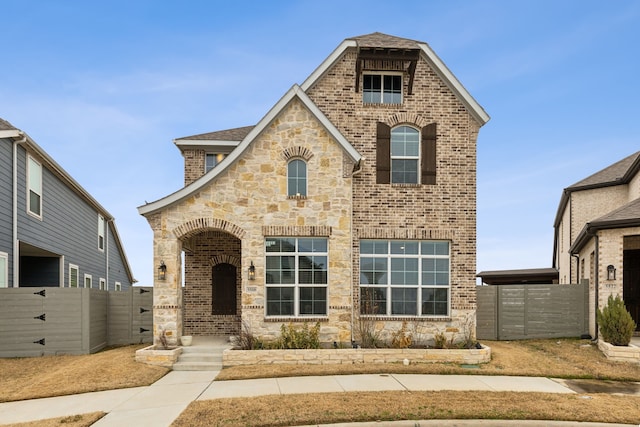 french provincial home with a gate, brick siding, and fence