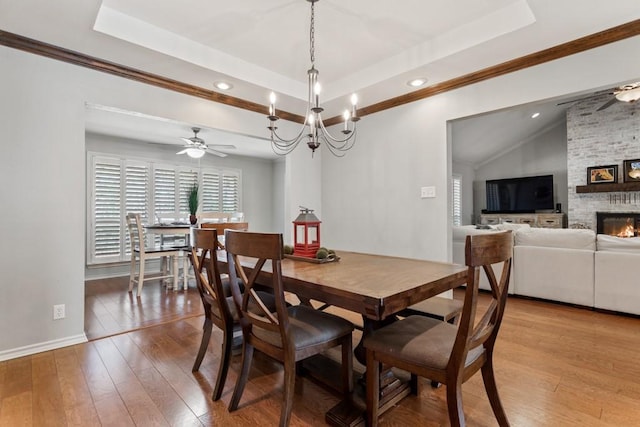 dining space with light wood-style floors, a fireplace, a tray ceiling, and a ceiling fan