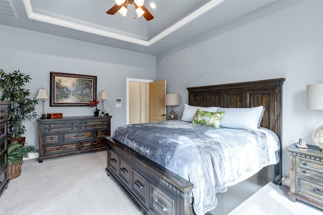 bedroom with light carpet, visible vents, a tray ceiling, and a ceiling fan